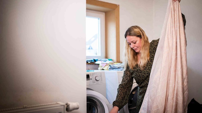 Elke staat voor haar wasmachine en droogkast met een laken in haar hand